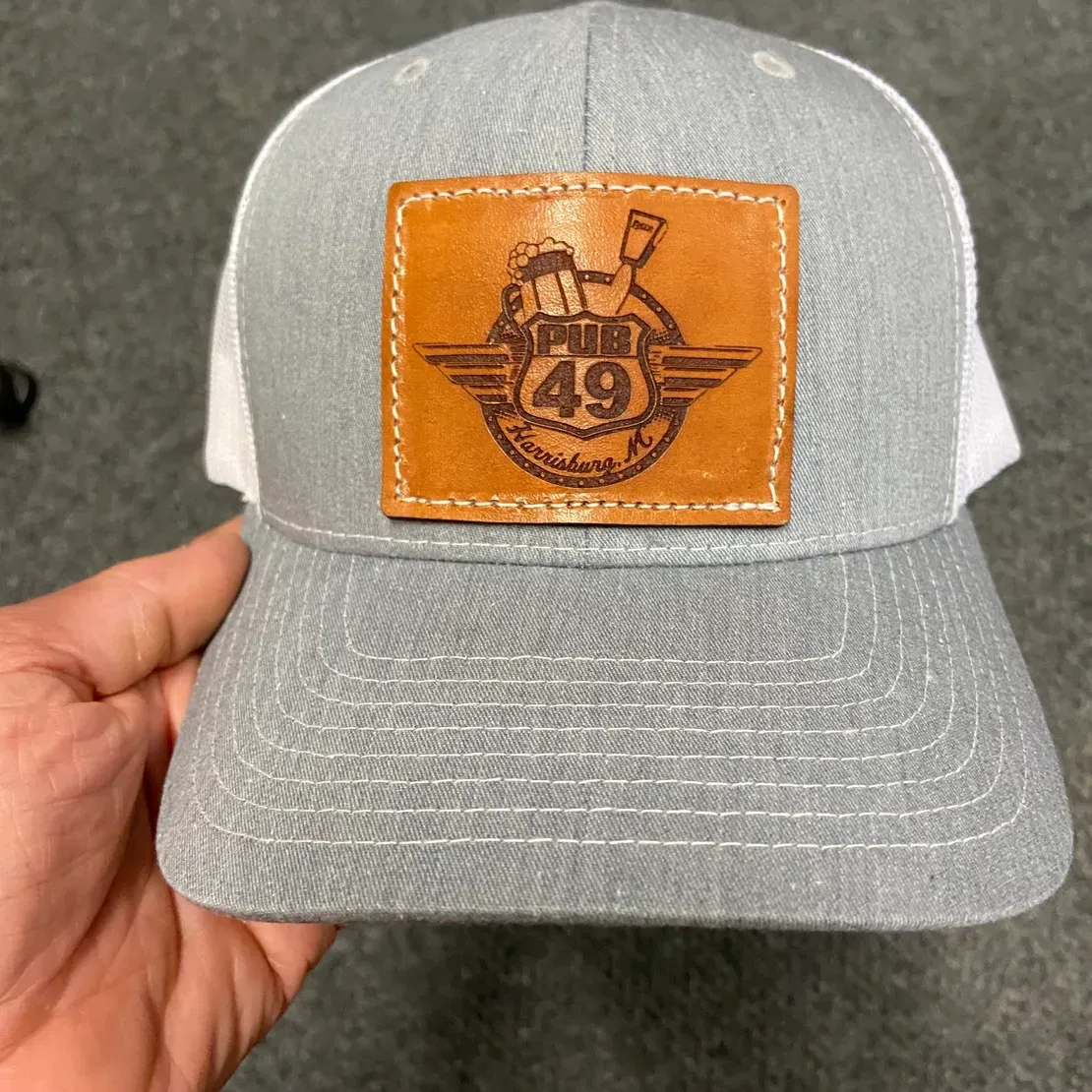Hand holding gray cap with leather emblem