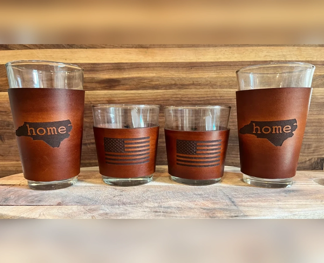 Set of four personalized pint glasses with the word "home" on them, placed on a wooden surface